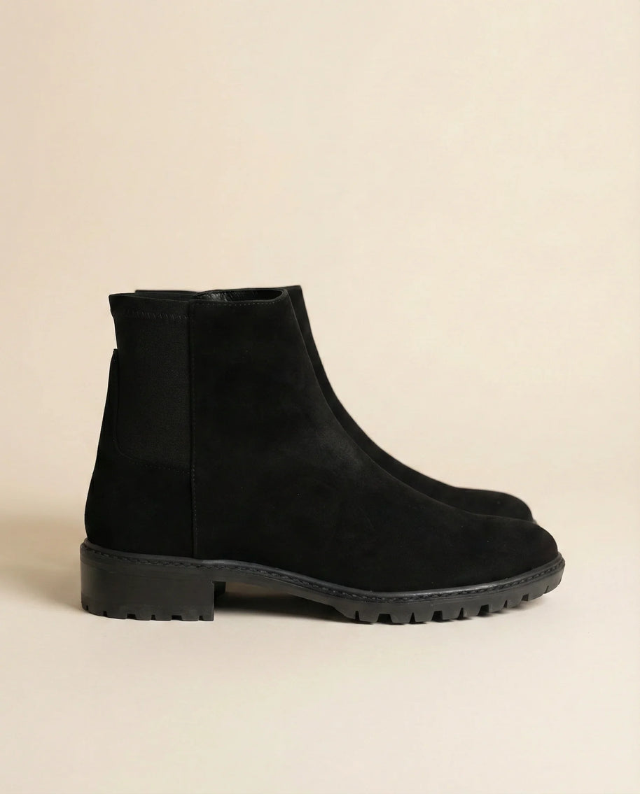 Black suede ankle boots with chunky rubber sole on beige background