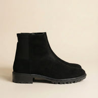 Black suede ankle boots with chunky rubber sole on beige background
