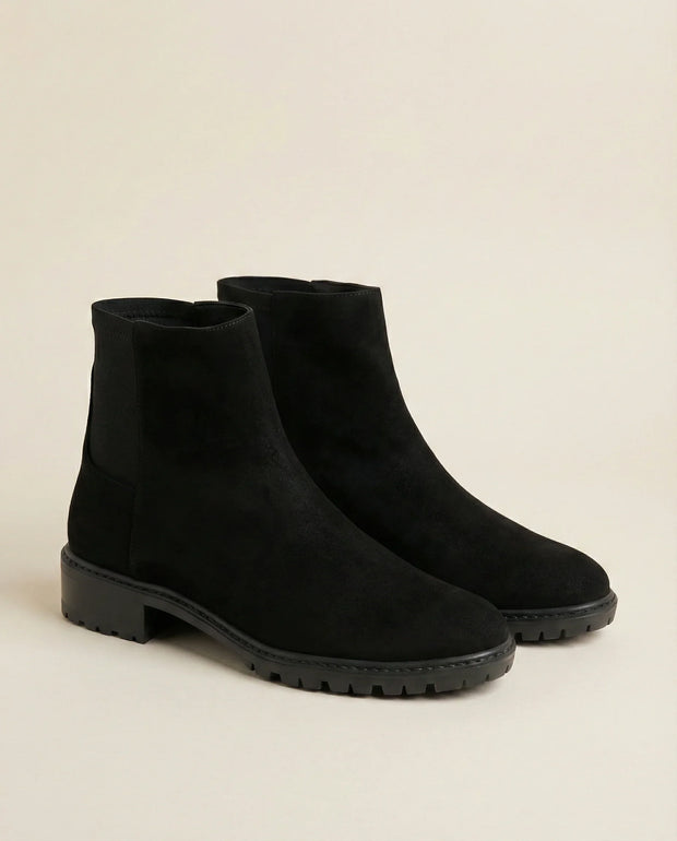 Black suede ankle boots with chunky soles on a neutral background