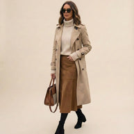 Woman in beige trench coat, cream turtleneck, brown skirt, black boots, holding tote bag