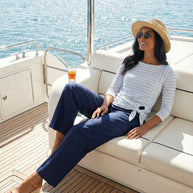 Woman in striped shirt and hat relaxing on yacht deck, enjoying sunny ocean view