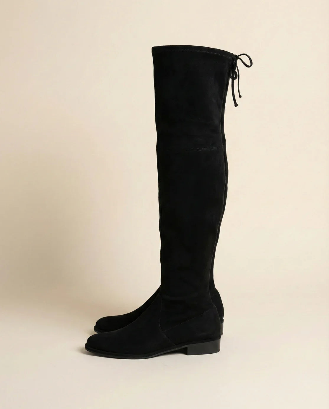 Black suede over-the-knee boots with low heels and tie detail on a neutral background