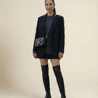Woman in black blazer, gray sweater, mini skirt, and over-the-knee black boots with crossbody bag