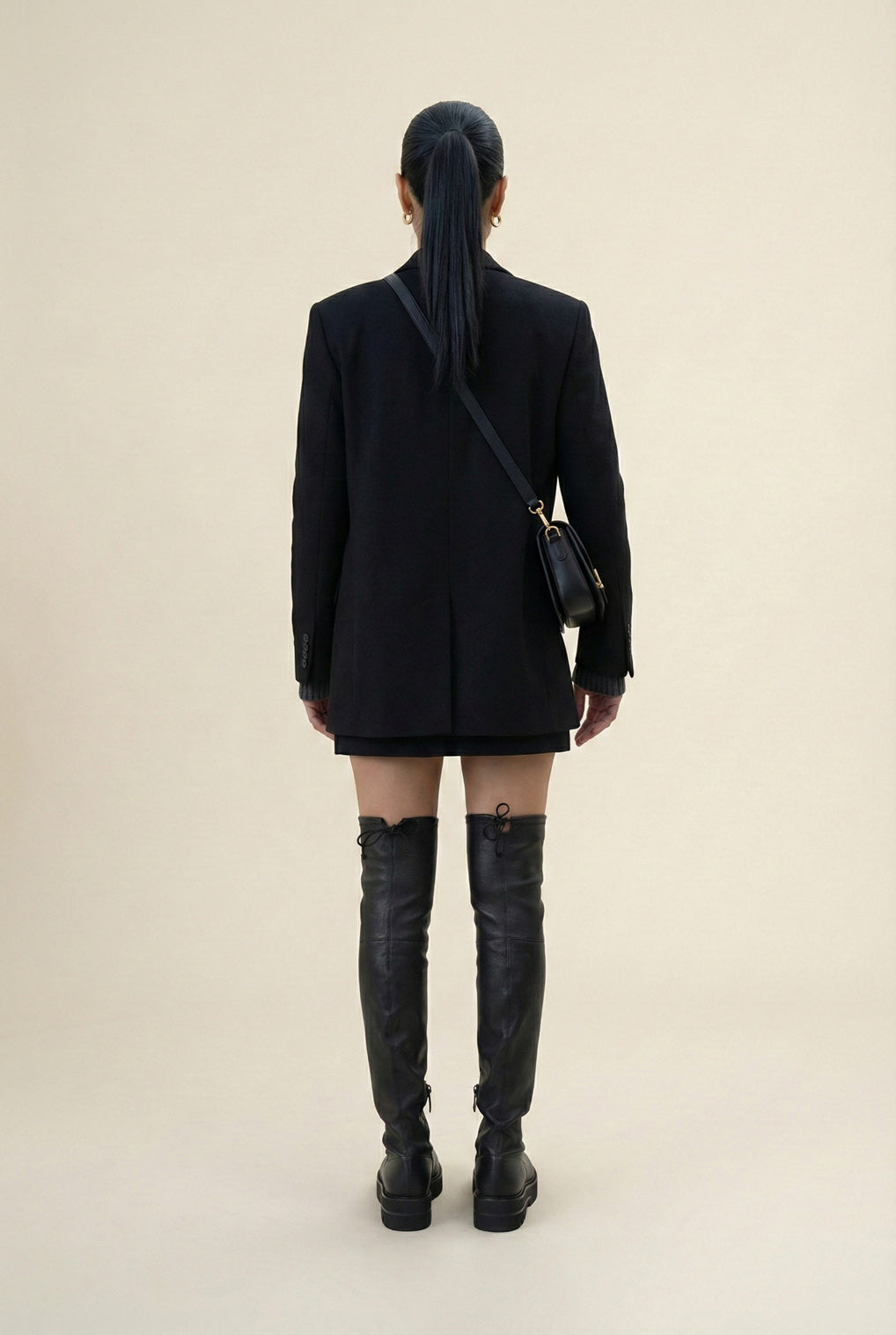 Woman in black blazer and mini skirt with black over-the-knee boots and crossbody bag