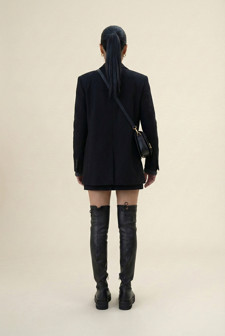 Woman in black blazer and mini skirt with black over-the-knee boots and crossbody bag