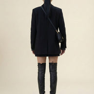 Woman in black blazer and mini skirt with black over-the-knee boots and crossbody bag