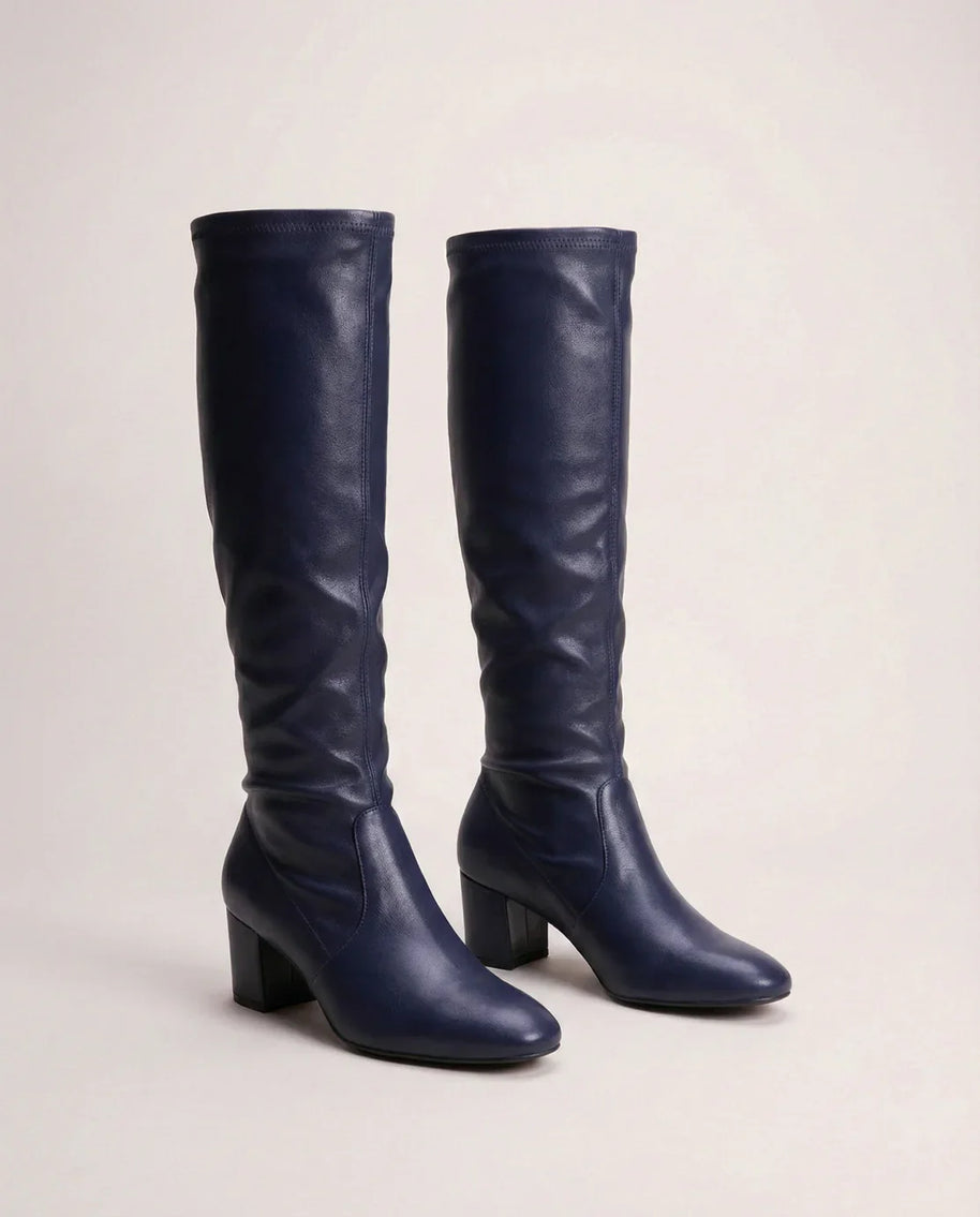 Pair of navy blue knee-high leather boots with block heels on neutral background
