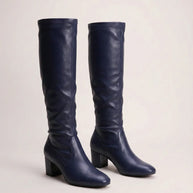 Pair of navy blue knee-high leather boots with block heels on neutral background