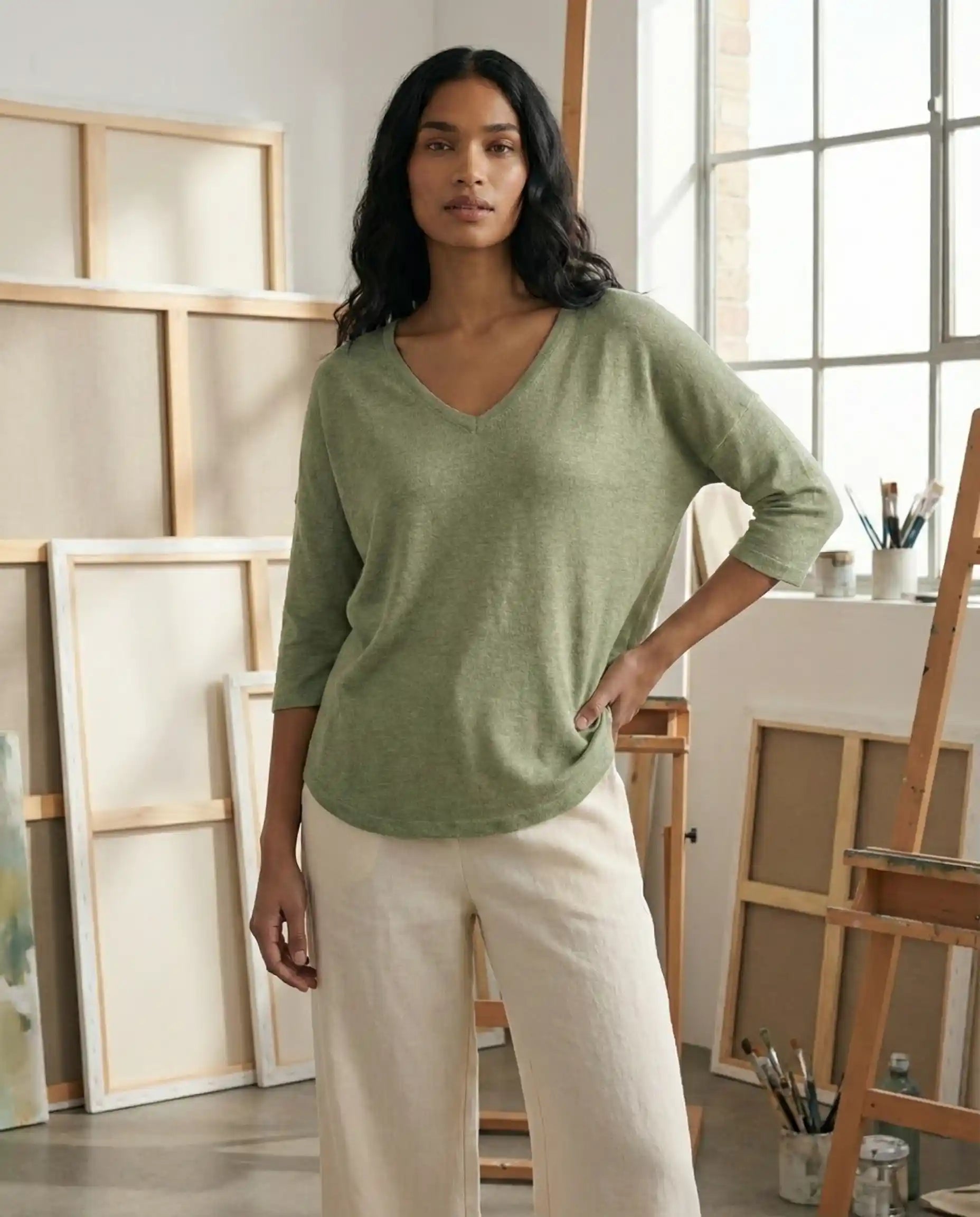 Woman in a light green V-neck top and cream pants standing in an artist studio