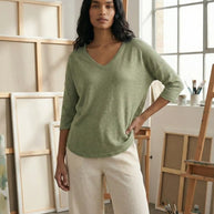 Woman in a light green V-neck top and cream pants standing in an artist studio