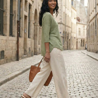 Woman in green top and beige wide-leg pants walking on a cobblestone street with a brown tote