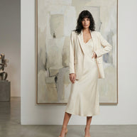 Woman in cream blazer and satin slip dress posing in modern minimalist room with abstract art