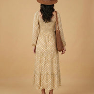 Woman in beige polka dot midi dress, straw hat, woven bag, heels, neutral background