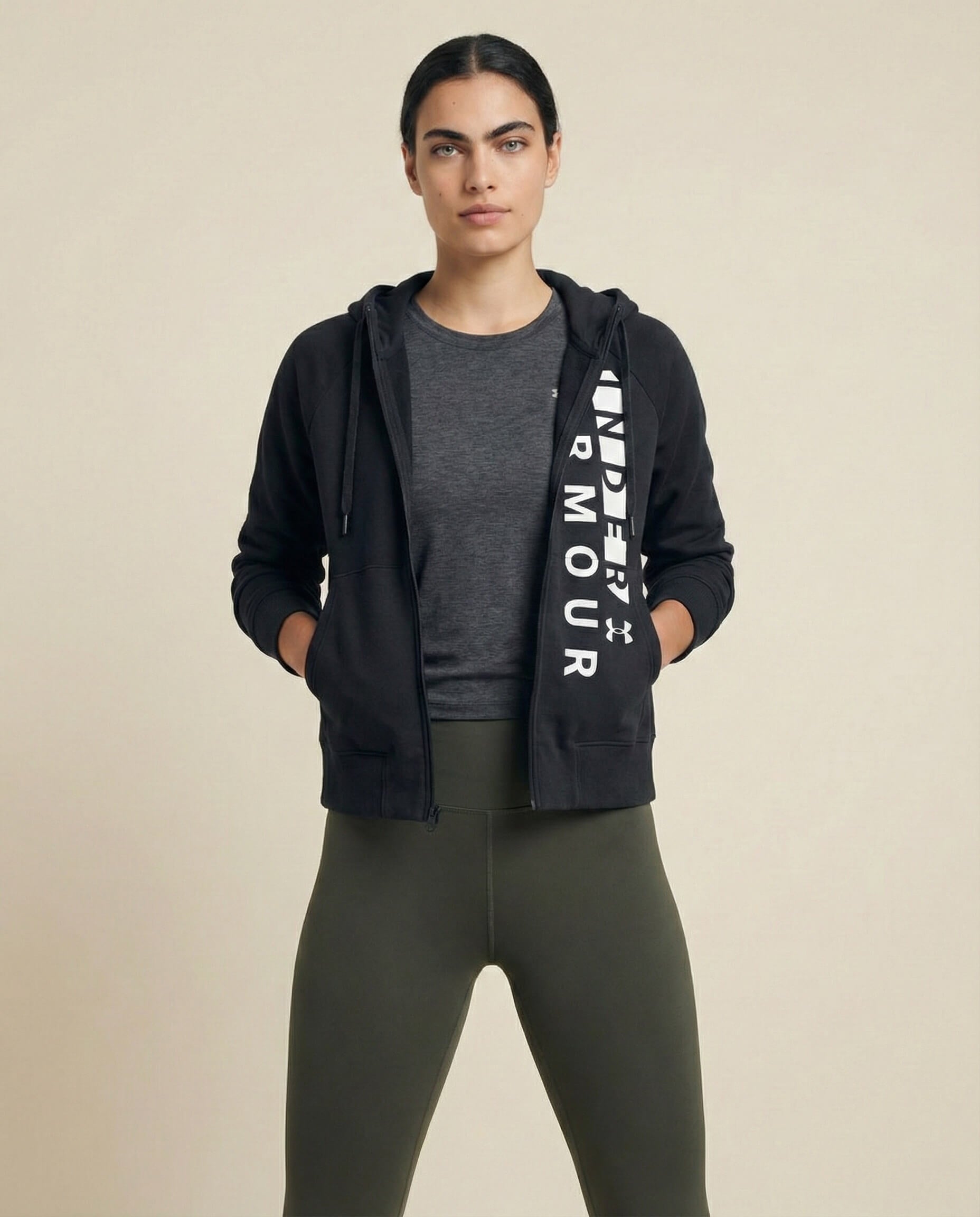 Woman wearing black zip-up hoodie with white lettering, grey t-shirt, and olive leggings