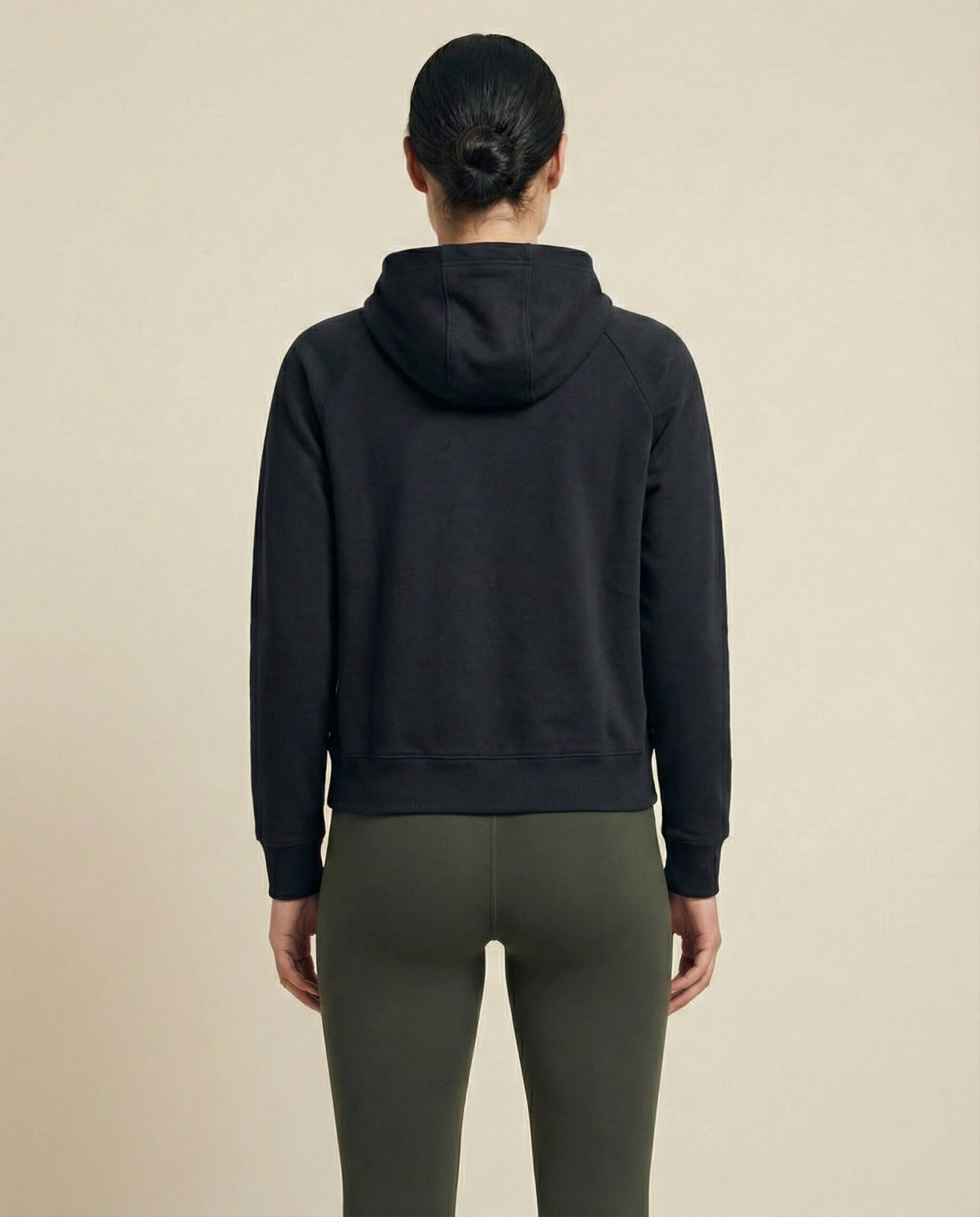 Woman in black hoodie and olive leggings standing with back to camera