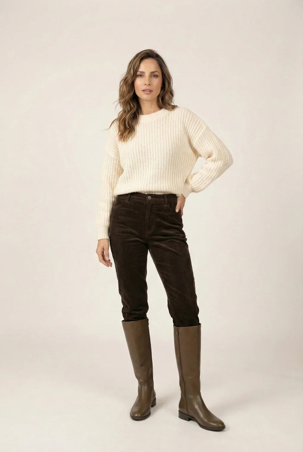 Woman in cream knit sweater, brown corduroy pants, and knee-high brown boots