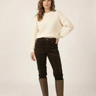 Woman in cream knit sweater, brown corduroy pants, and knee-high brown boots