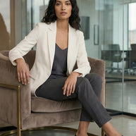 Woman in white blazer, charcoal pants, and loafers sitting in a modern office chair
