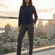 Woman in navy blazer and gray trousers on rooftop at sunset, city skyline background