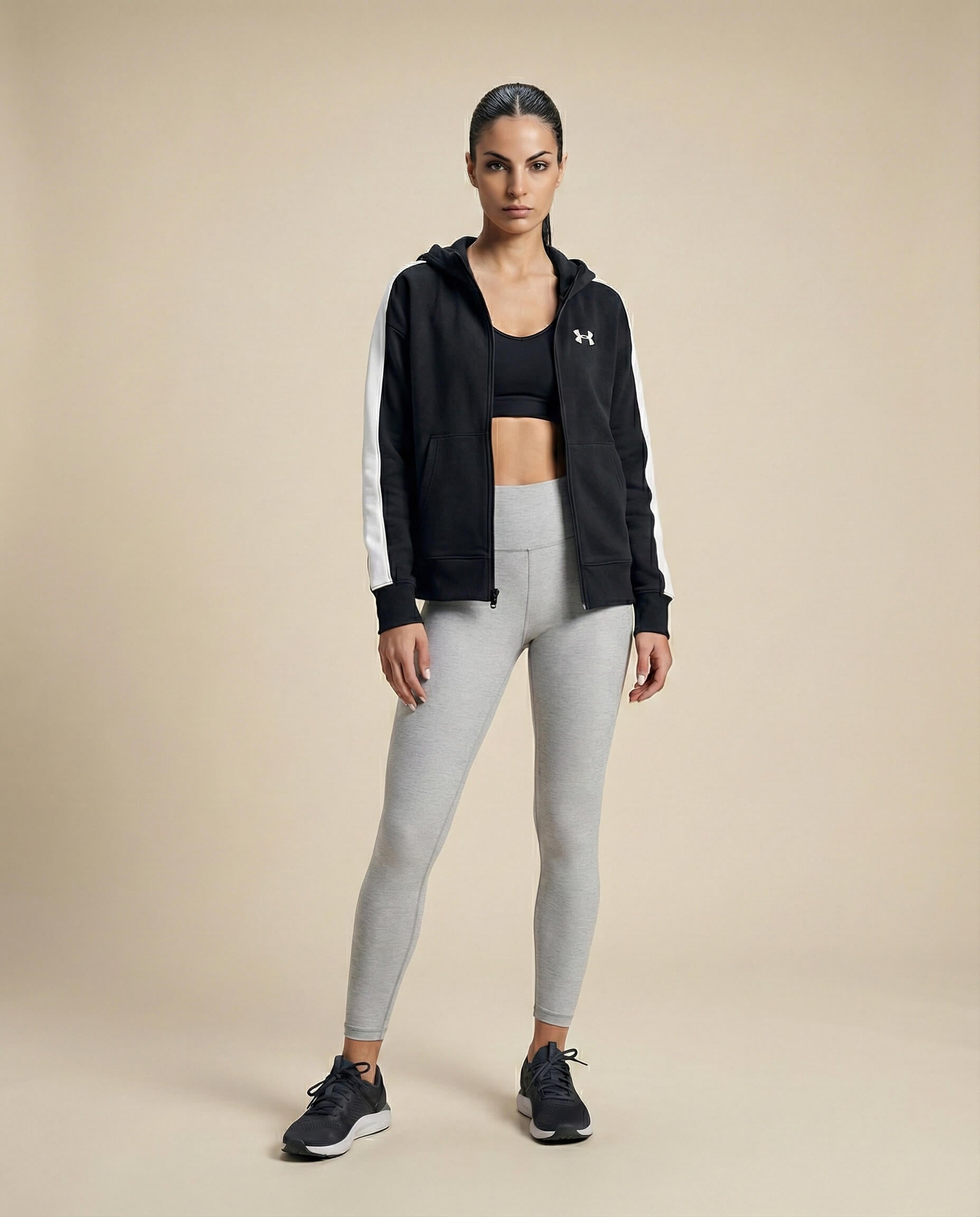 Woman in athleisure wear with black zip-up hoodie, sports bra, gray leggings, black sneakers