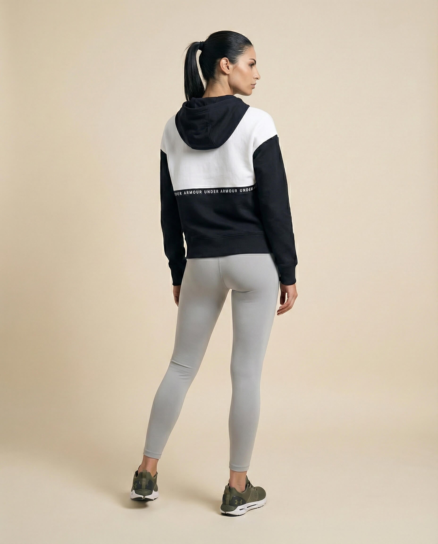 Woman in black and white hoodie, gray leggings, green sneakers, standing against beige backdrop