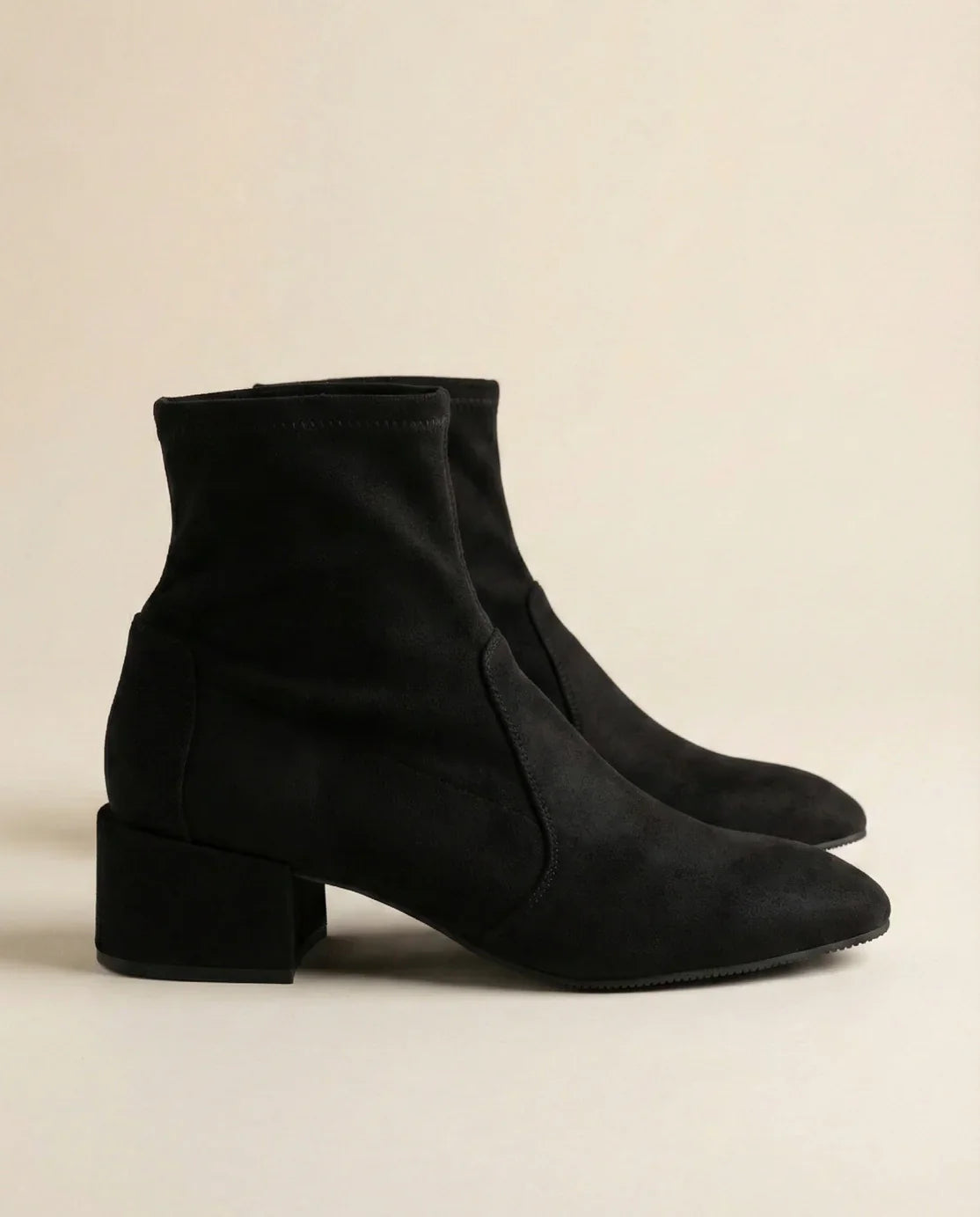 Pair of black suede ankle boots with block heels on a neutral background