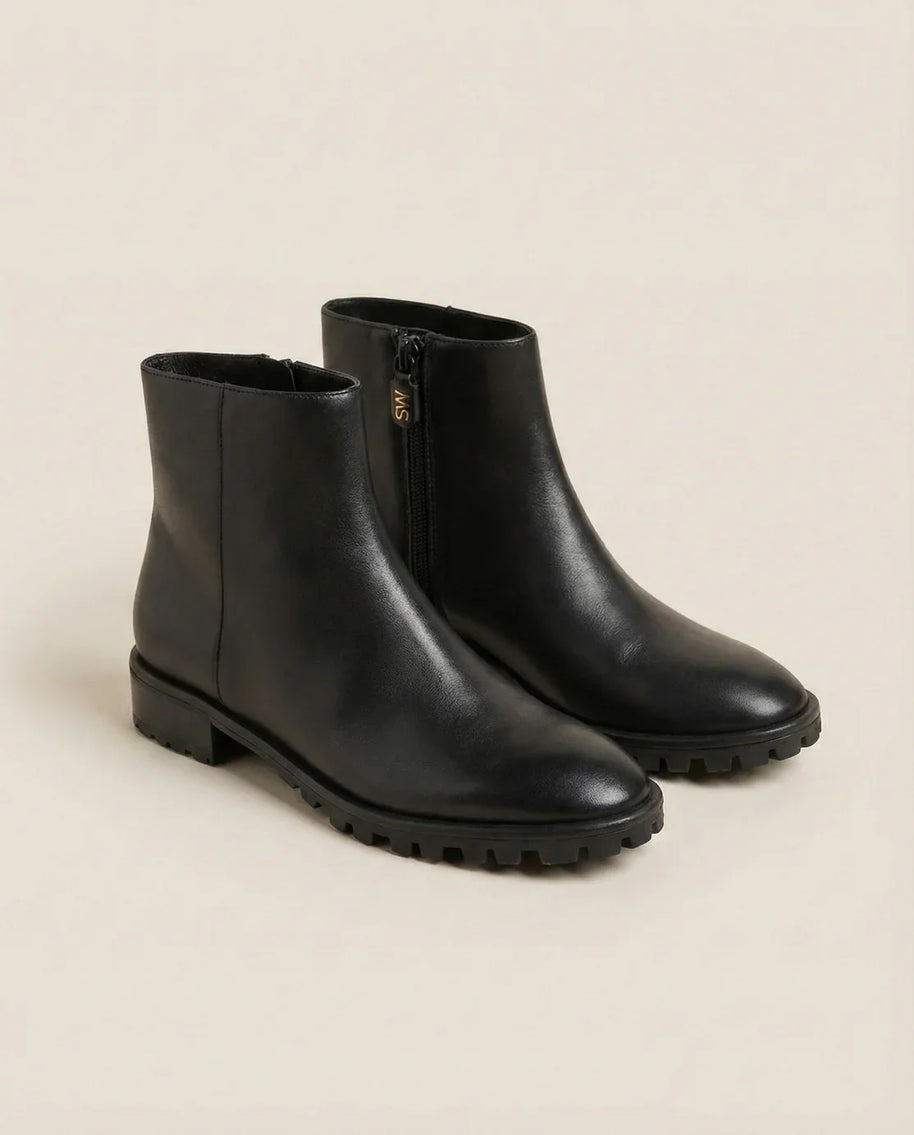 Black ankle boots with side zipper and chunky sole on neutral background
