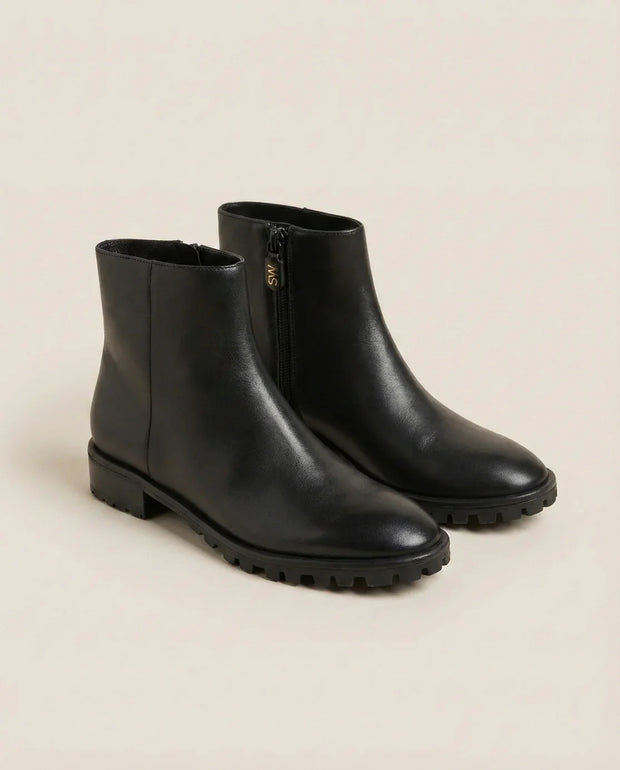 Black ankle boots with side zipper and chunky sole on neutral background