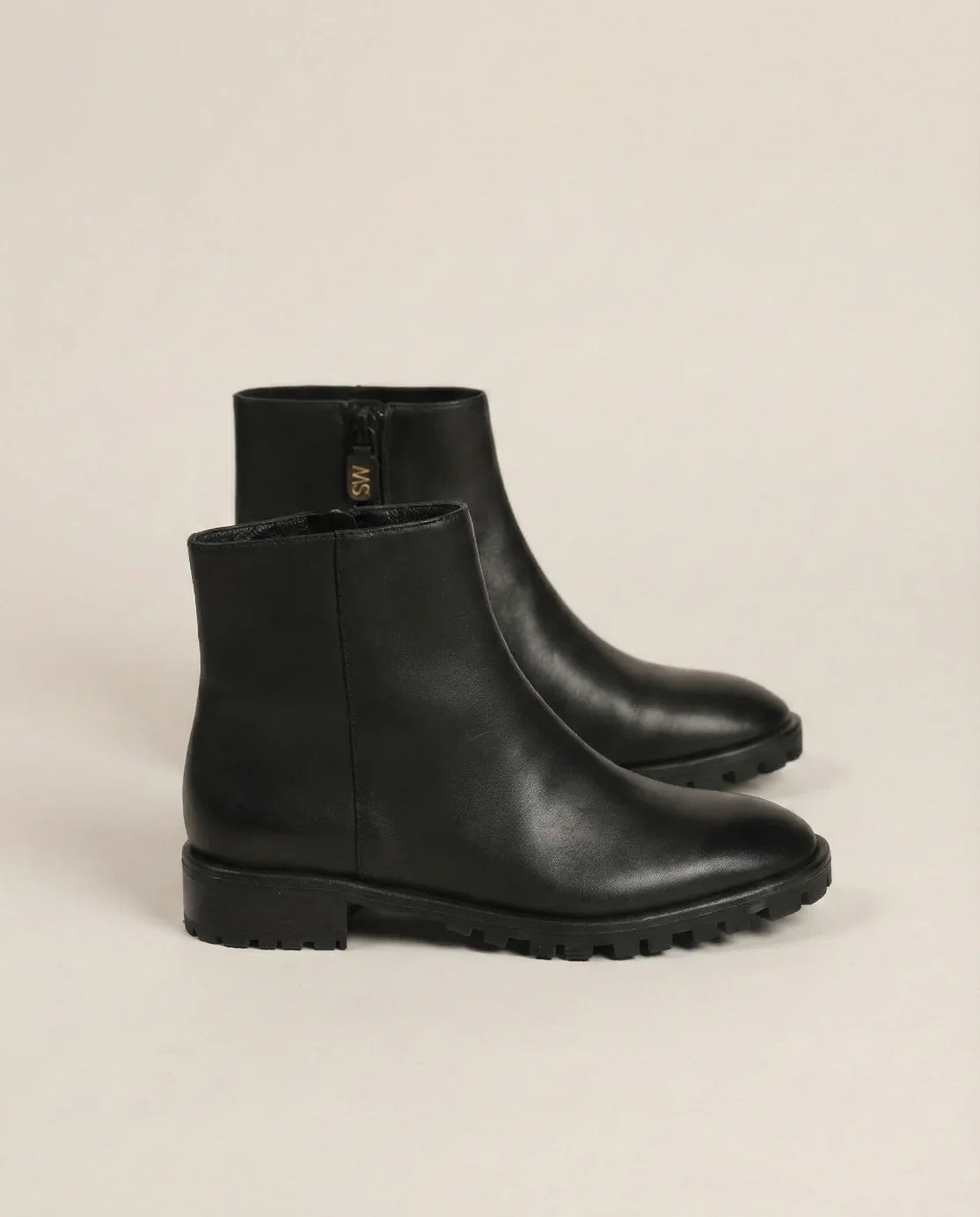 Black leather ankle boots with side zipper and lug sole on light background