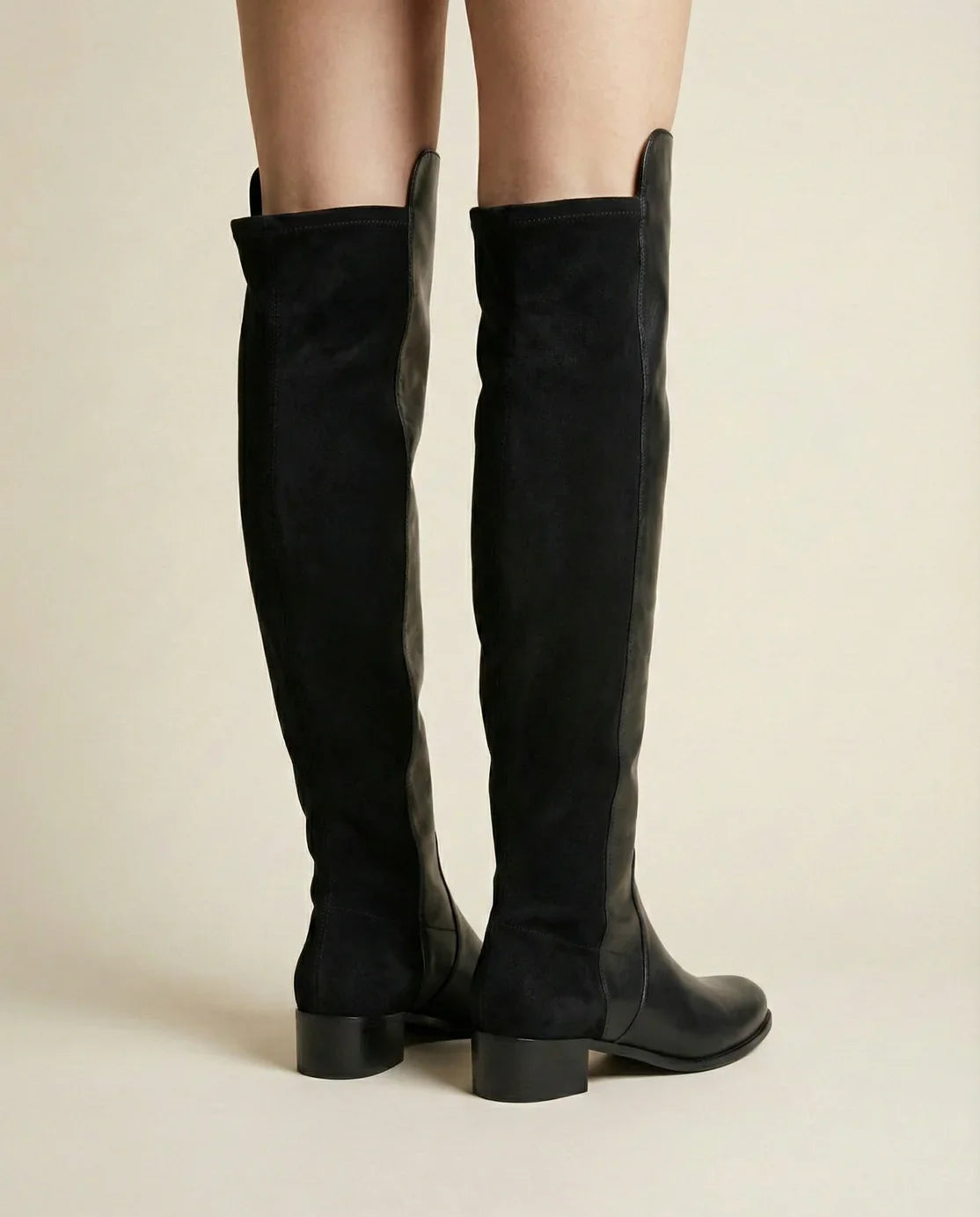 Black knee-high suede boots with block heels on a neutral background