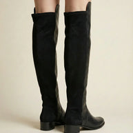 Black knee-high suede boots with block heels on a neutral background