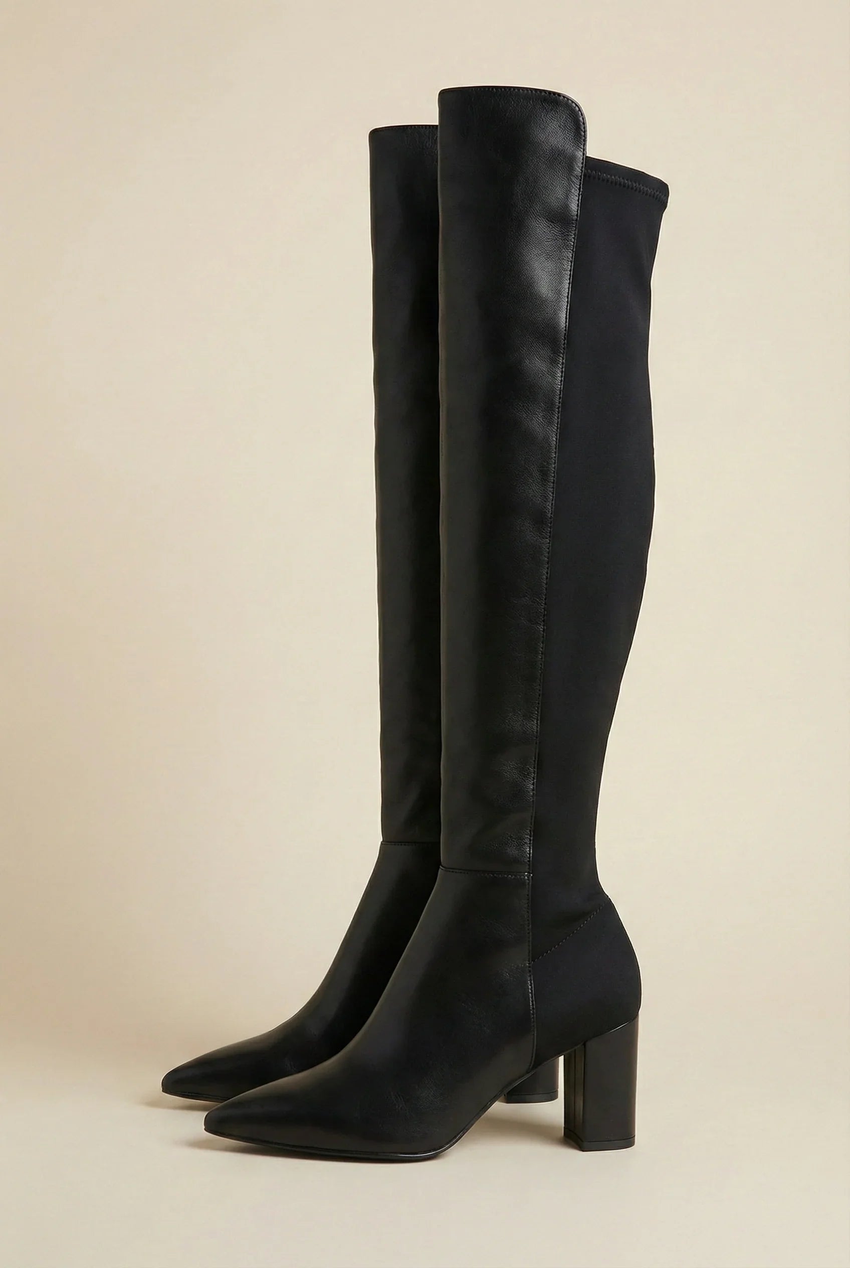 Black knee-high heeled boots with pointed toes on a neutral background
