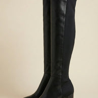 Black knee-high heeled boots with pointed toes on a neutral background