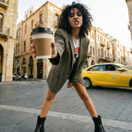 Woman in blazer and boots holding coffee cup on urban street with historic buildings and taxi