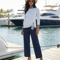 Woman in striped long sleeve top, wide-leg navy pants, straw hat and sunglasses by yachts