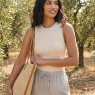 Woman wearing beige sleeveless top, drawstring pants, and straw tote bag outdoors