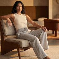 Woman in a sleeveless ribbed top and linen pants sitting on a modern accent chair indoors