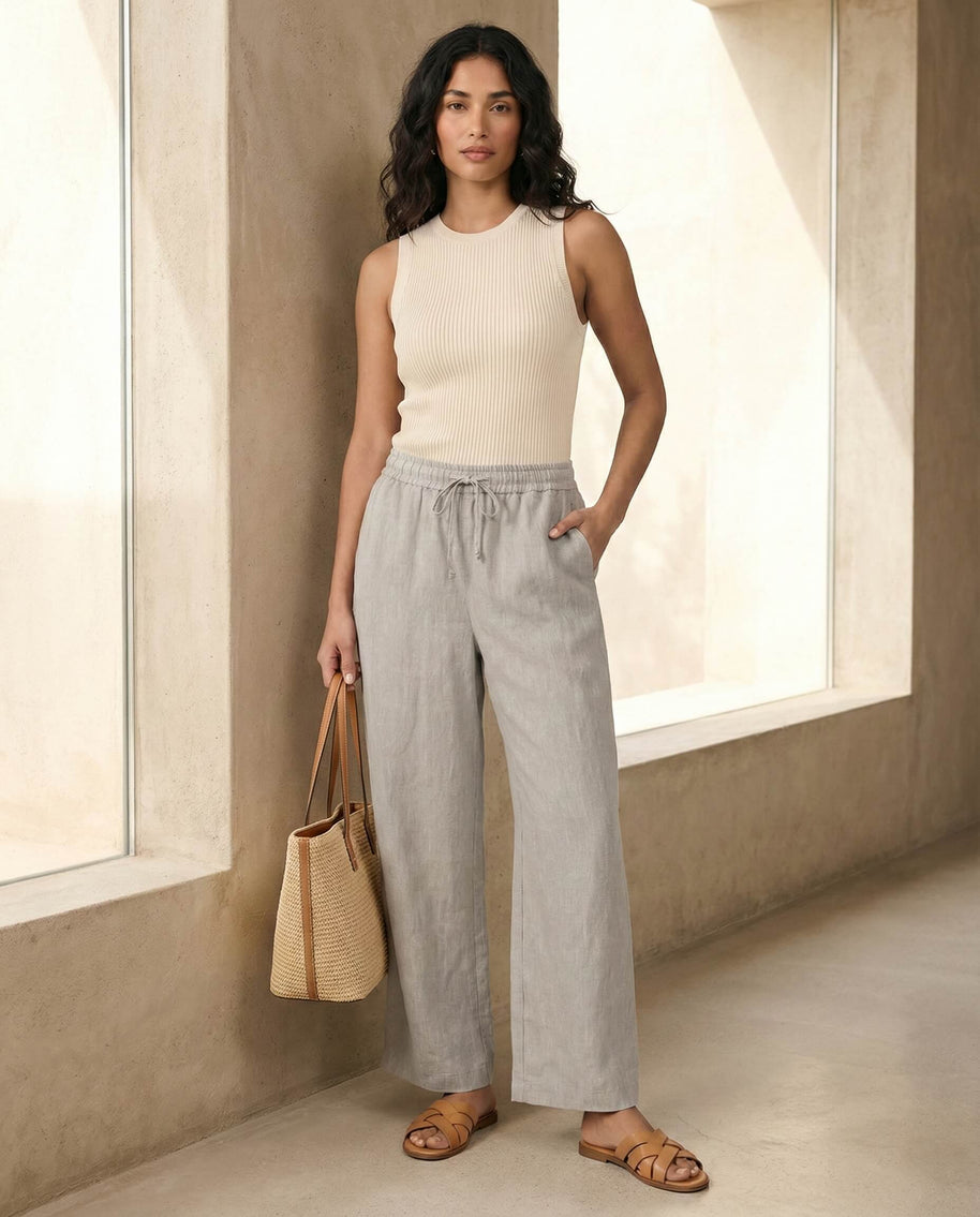 Woman in beige sleeveless ribbed top, gray wide-leg pants, straw tote, and sandals