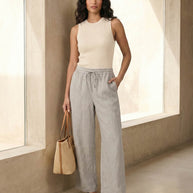 Woman in beige sleeveless ribbed top, gray wide-leg pants, straw tote, and sandals