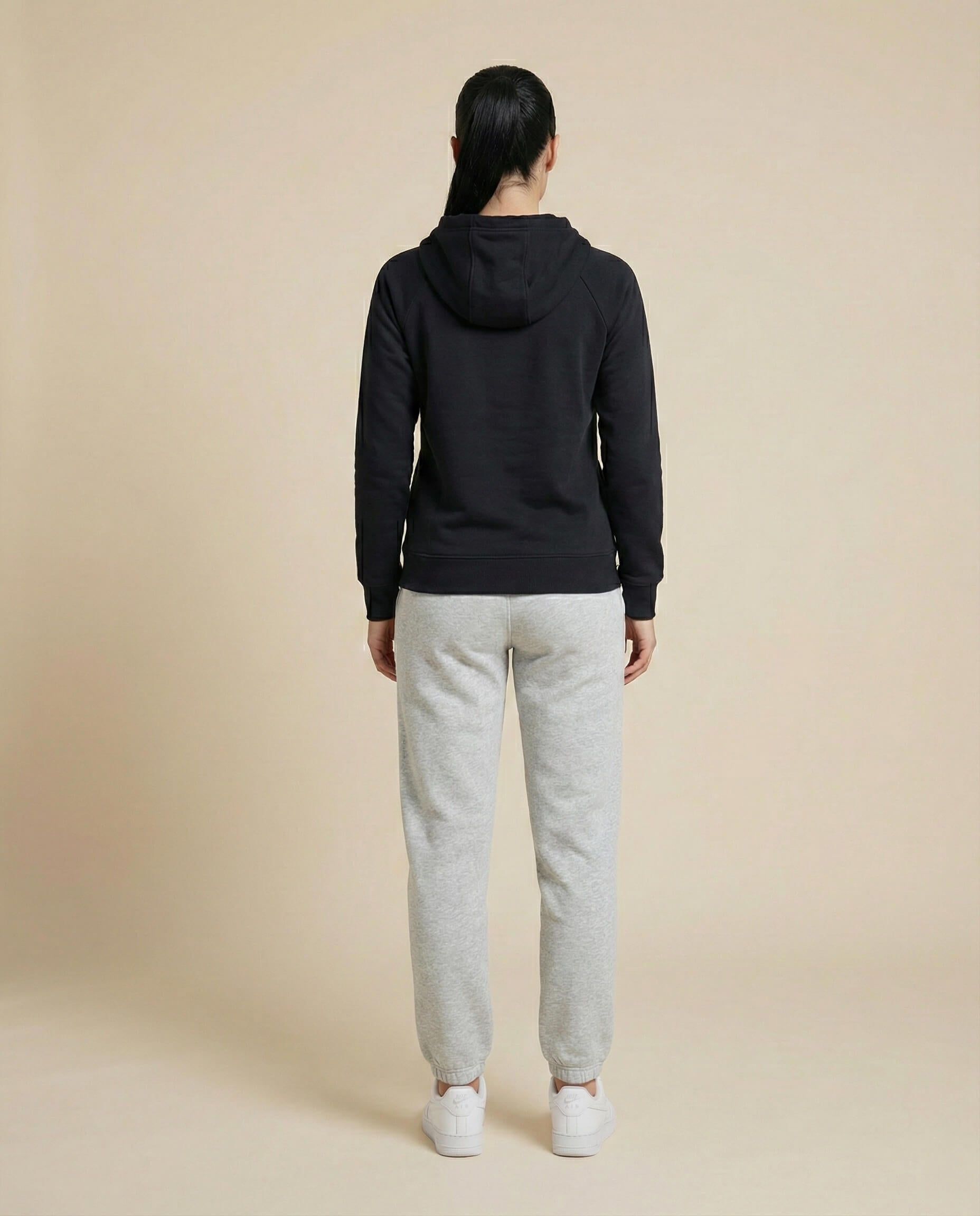 Woman in black hoodie and gray sweatpants, standing, back view, casual wear