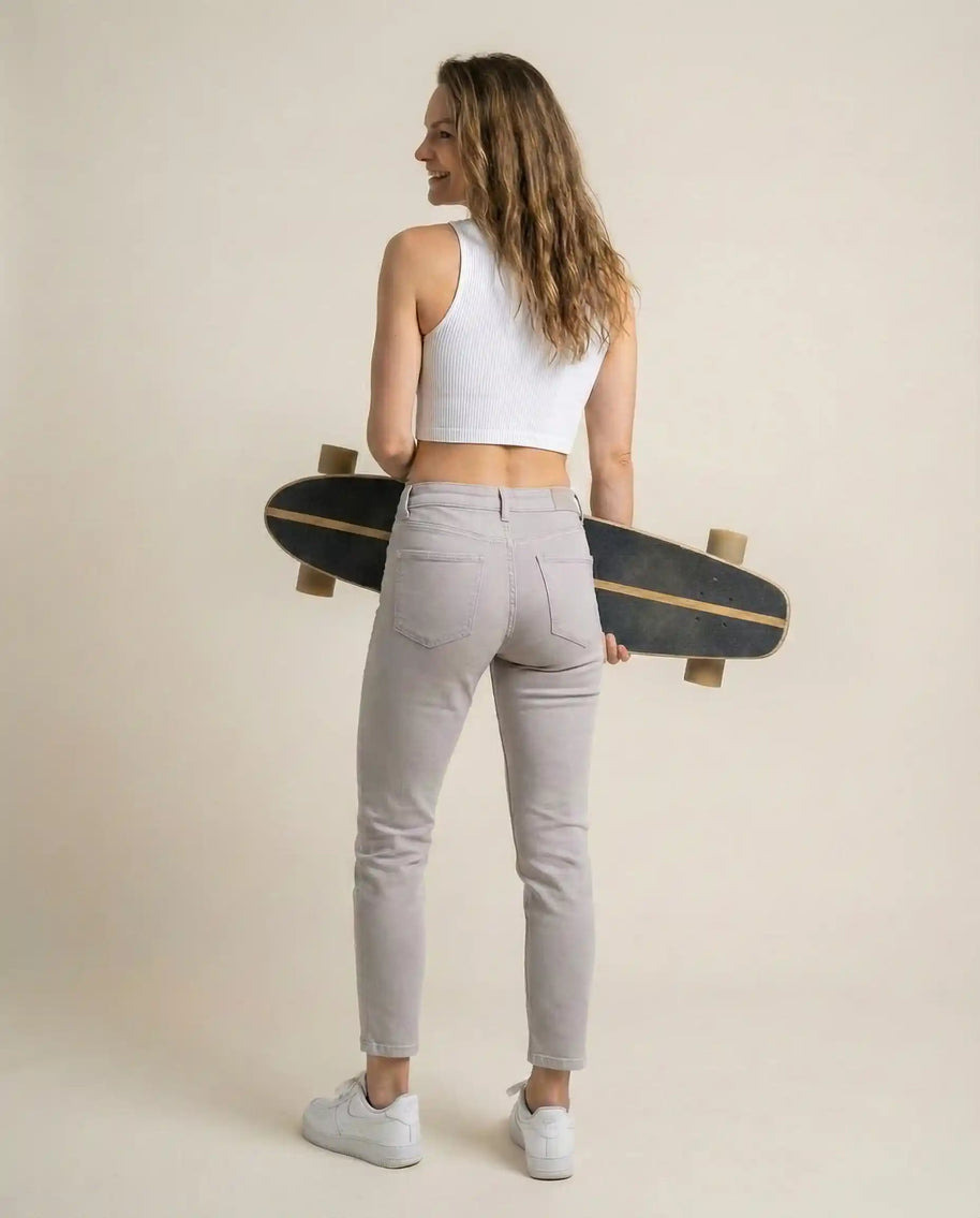 Woman in white crop top and light jeans holding skateboard, casual fashion style