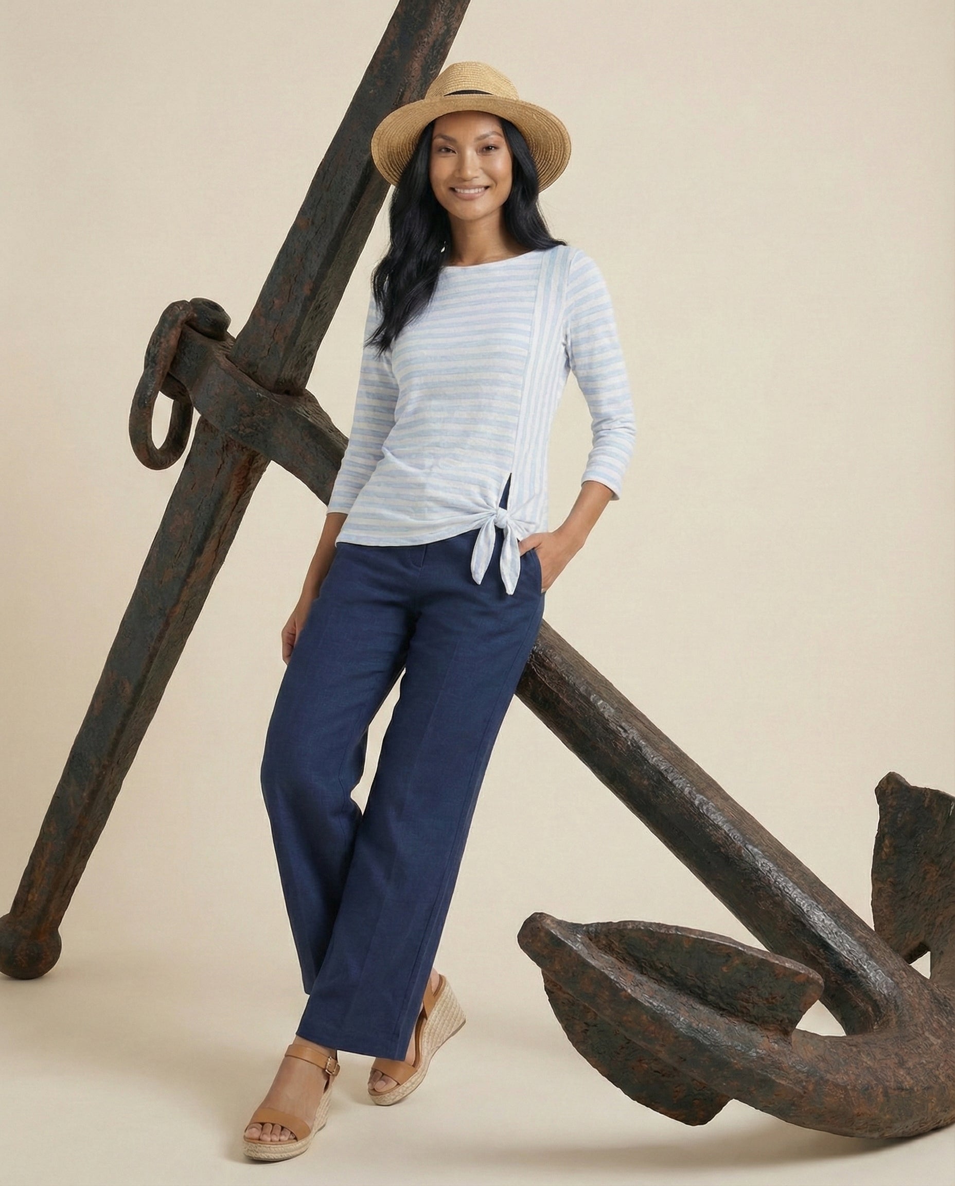 Woman in a straw hat, striped top, and navy pants posing by a large anchor
