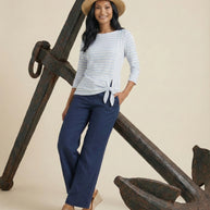 Woman in a straw hat, striped top, and navy pants posing by a large anchor
