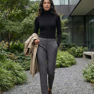 Woman in black turtleneck and gray trousers walking outdoors in modern garden setting