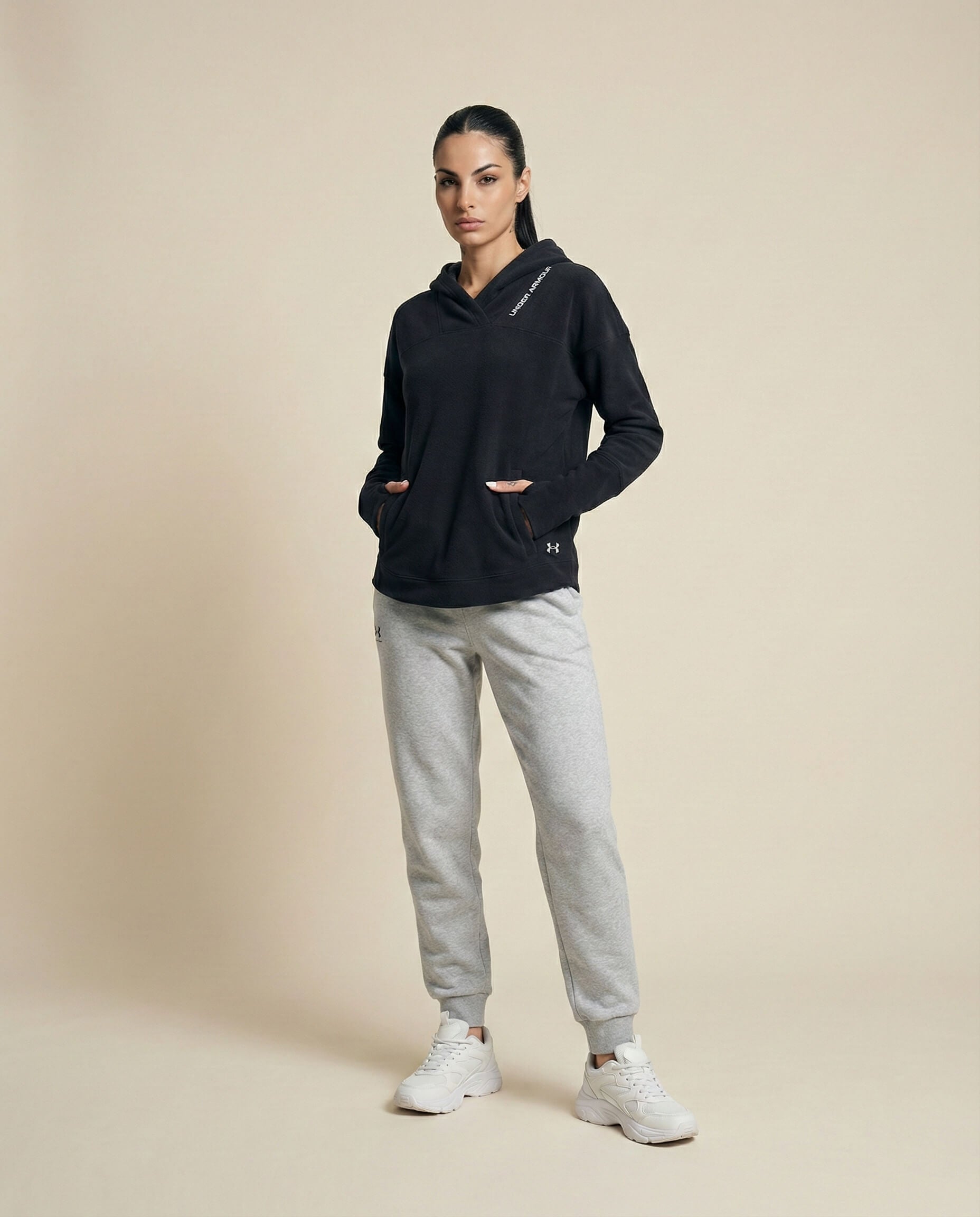 Woman wearing black hoodie, gray joggers, and white sneakers on beige background