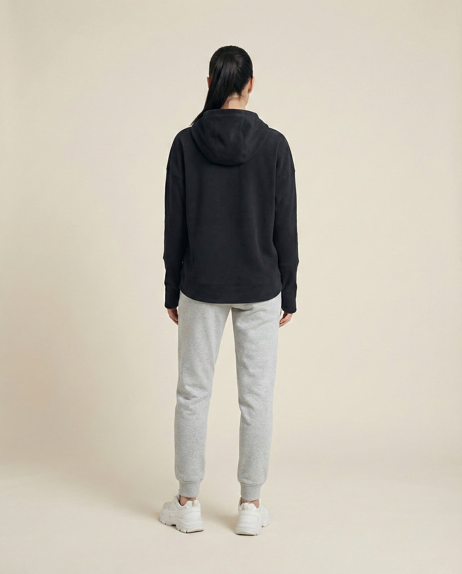 Woman in black hoodie and gray sweatpants standing in studio, casual loungewear outfit