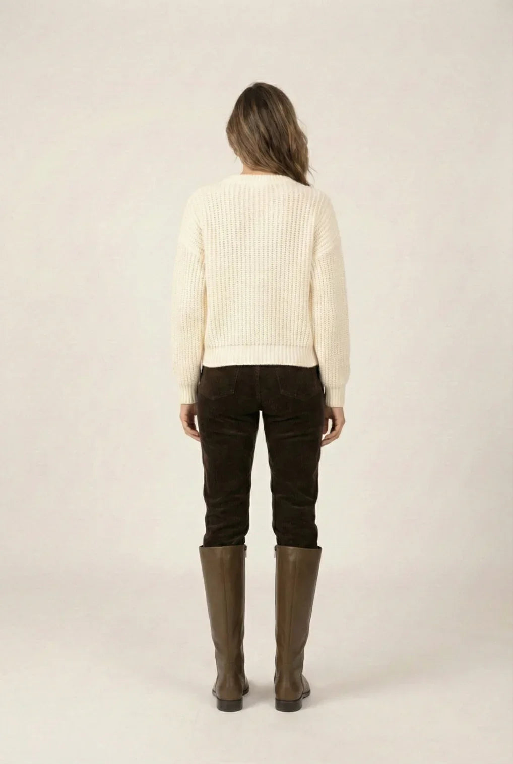 Woman in cream knit sweater, brown pants, and tall brown boots, back view
