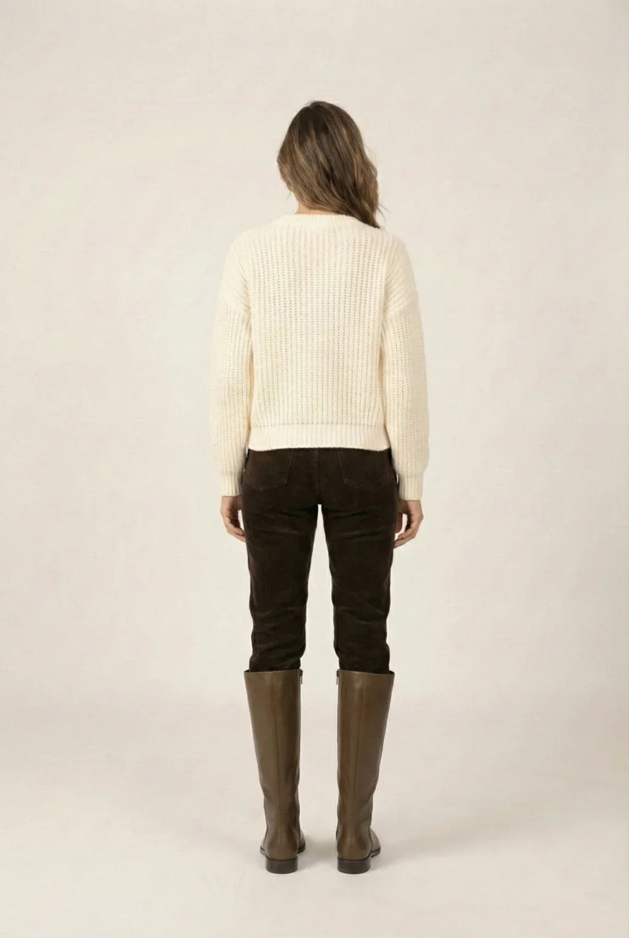 Woman in cream knit sweater, brown pants, and tall brown boots, back view