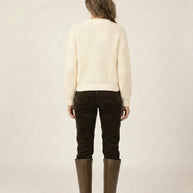 Woman in cream knit sweater, brown pants, and tall brown boots, back view