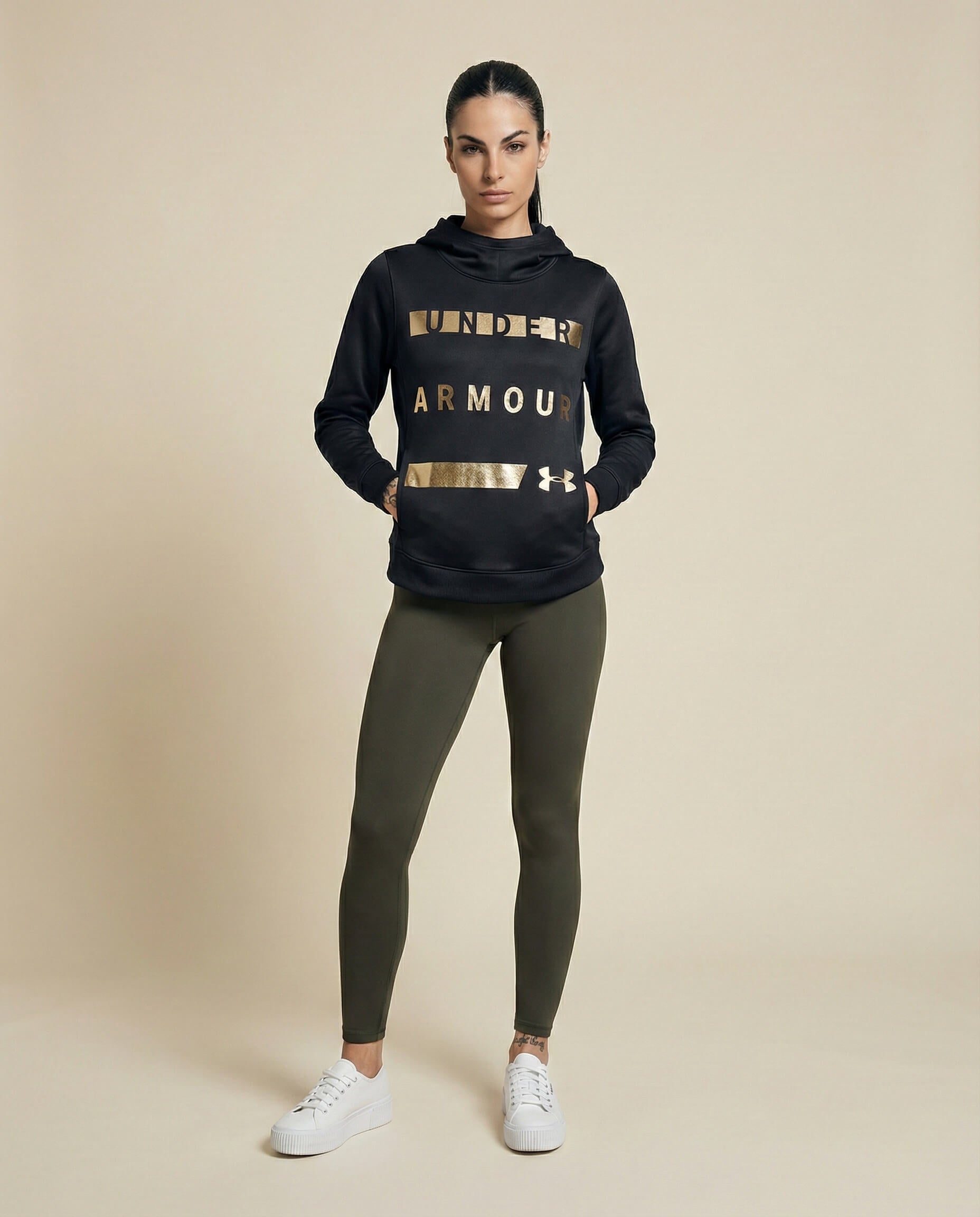 Woman in black Under Armour hoodie with gold lettering, olive leggings, and white sneakers